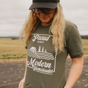 Woman in olive green proud to be a Modern Homesteader t-shirt in a field