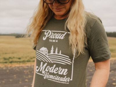 Woman in olive green proud to be a Modern Homesteader t-shirt in a field